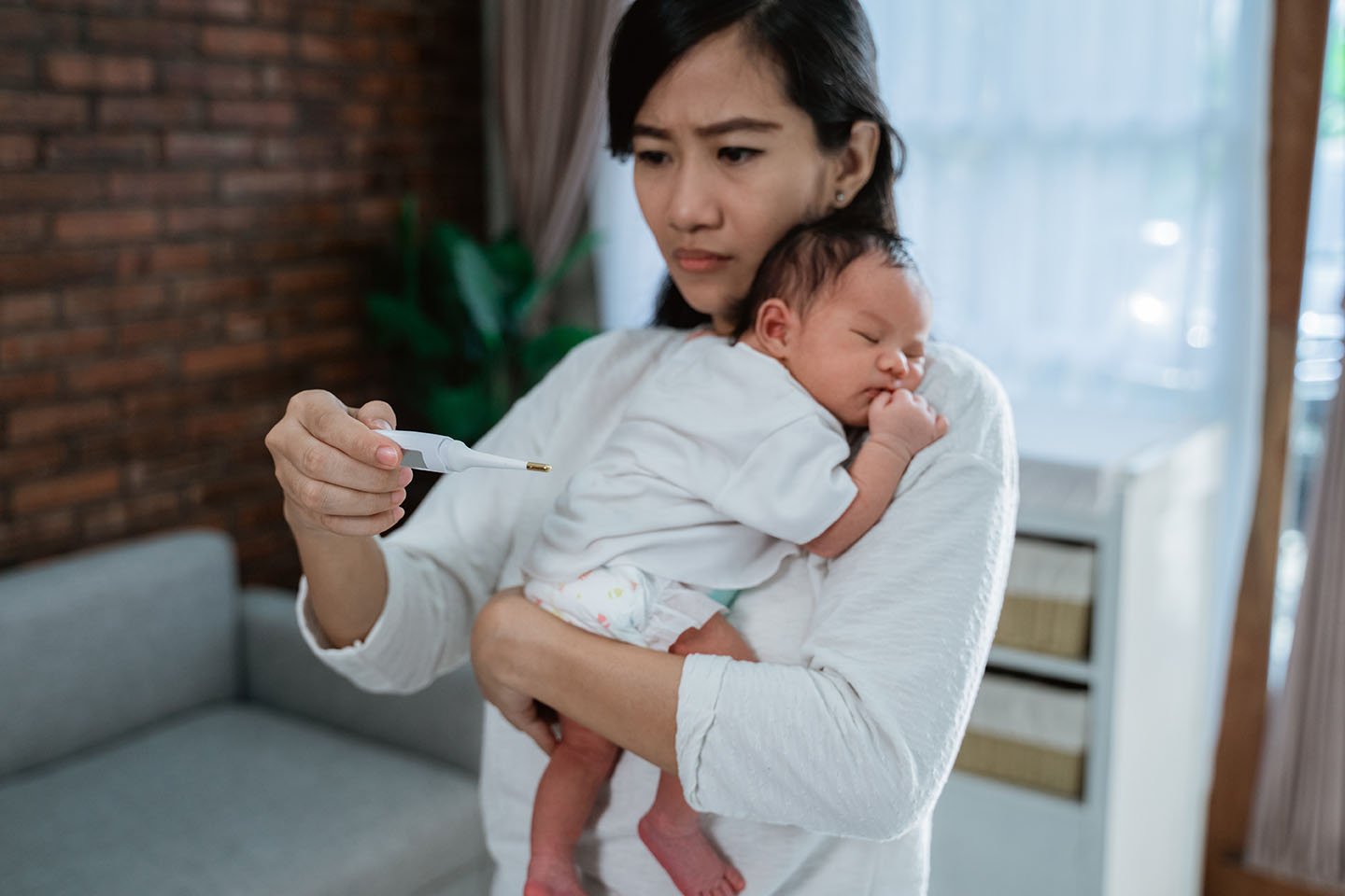 Mother holding infant and looking at thermometer.