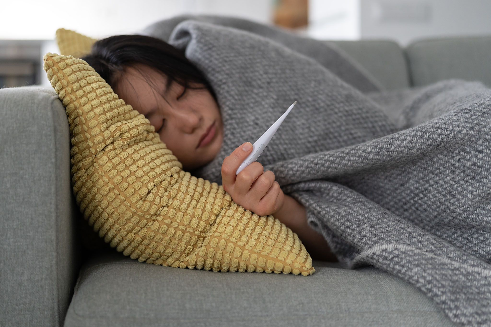 Young girl lying on a couch holding a thermometer.