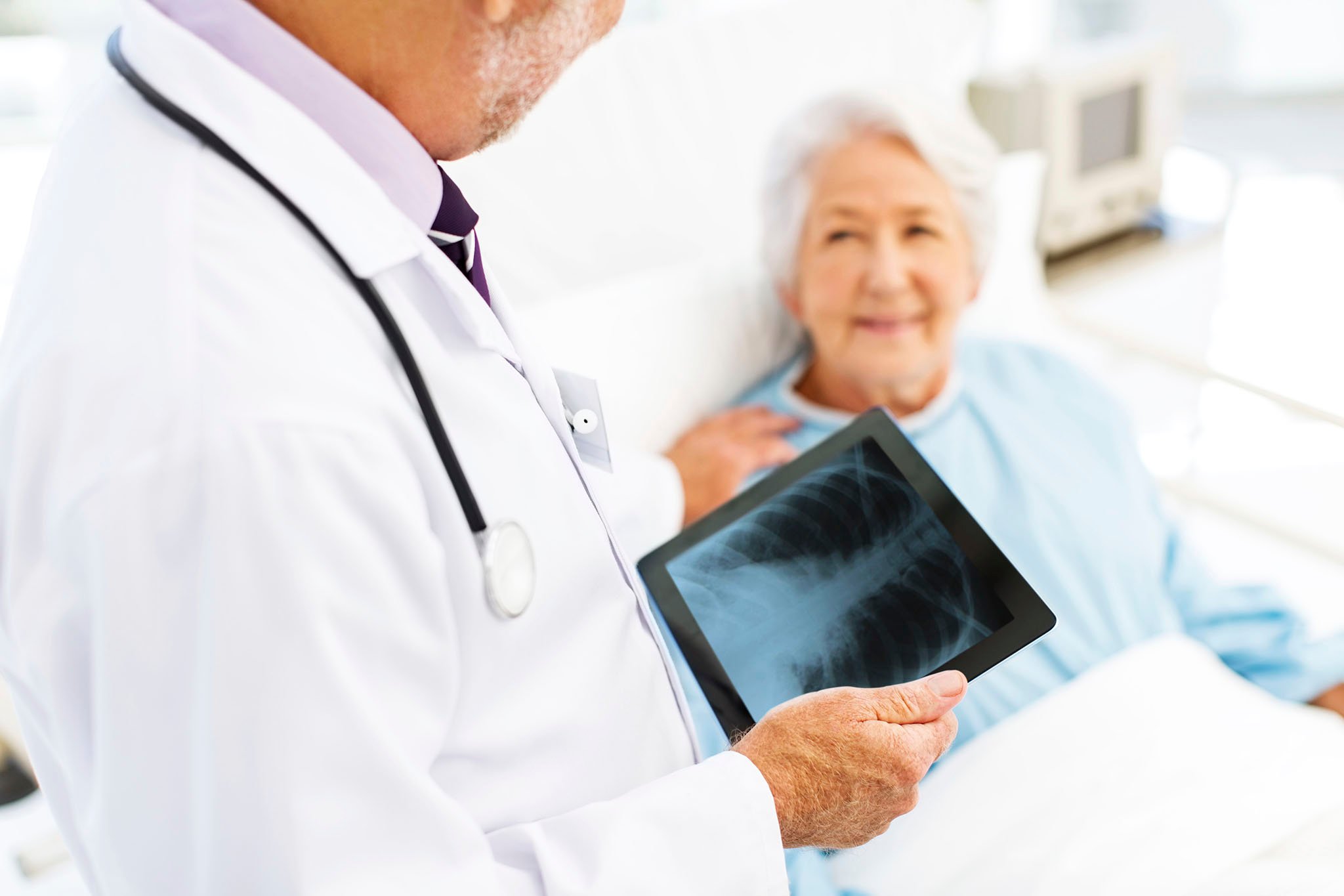 Physician reviewing X-ray with patient in hospital bed.