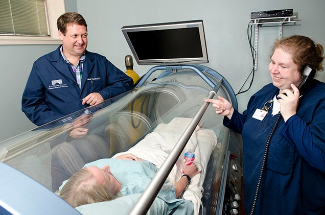 Physician and nurse with paitient who is inside a hyperbaric oxygen therapy chamber.