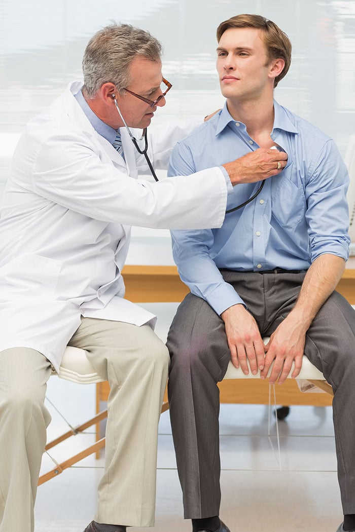 Male doctor examining young professional male with a stethoscope.