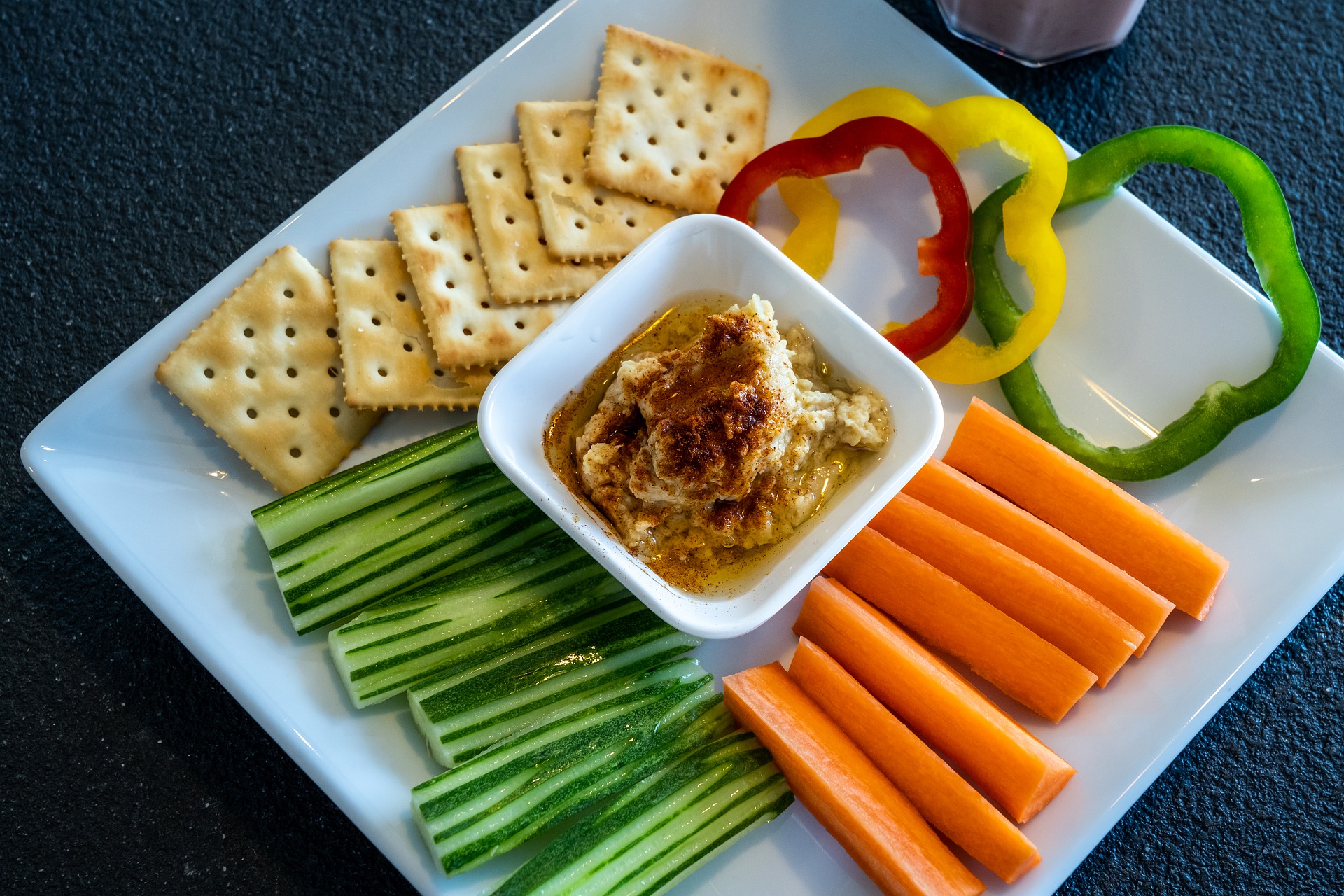 White plate with crackers, vegetables, and hummus.