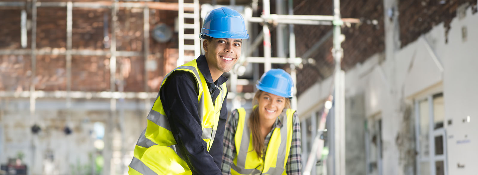 Young man and woman in hard hats and safety vests working on a job site.