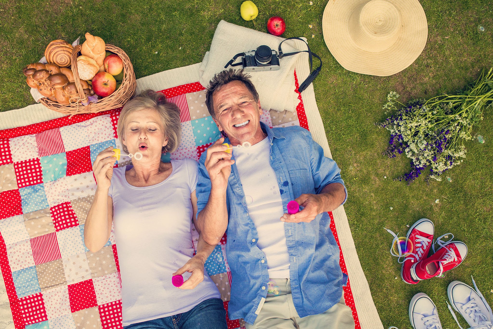 Middle-aged couple on picnic blanket blowing bubbles together